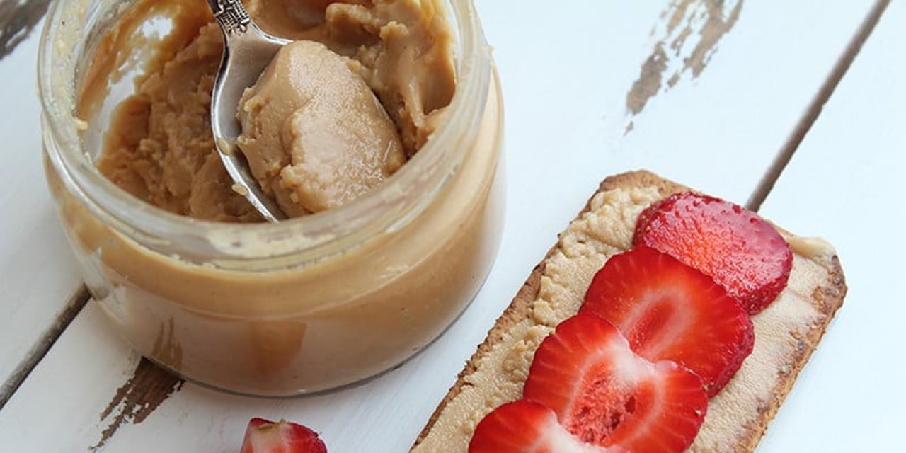 An open jar of peanut butter rests on a white wooden table. There