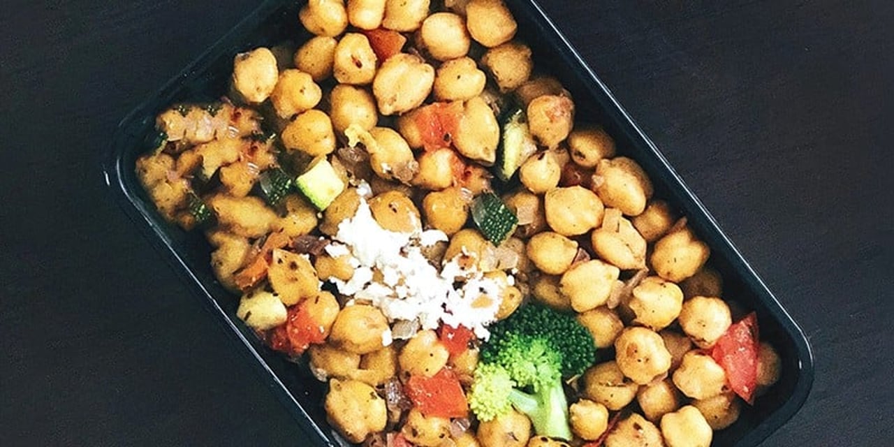 A rectangular baking tray filled to the heap with chickpeas. Mixed with the beans you can see herbs, and chunks of red pepper and broccoli.